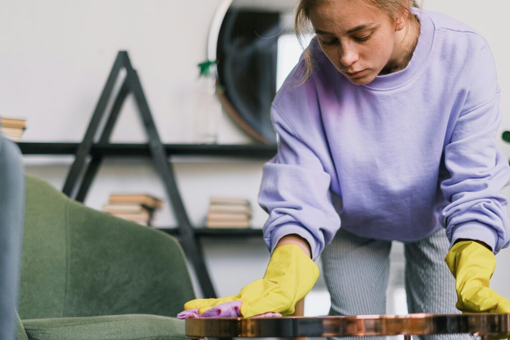 Focused young woman wearing gloves, cleaning a table in a stylish, modern apartment setting.